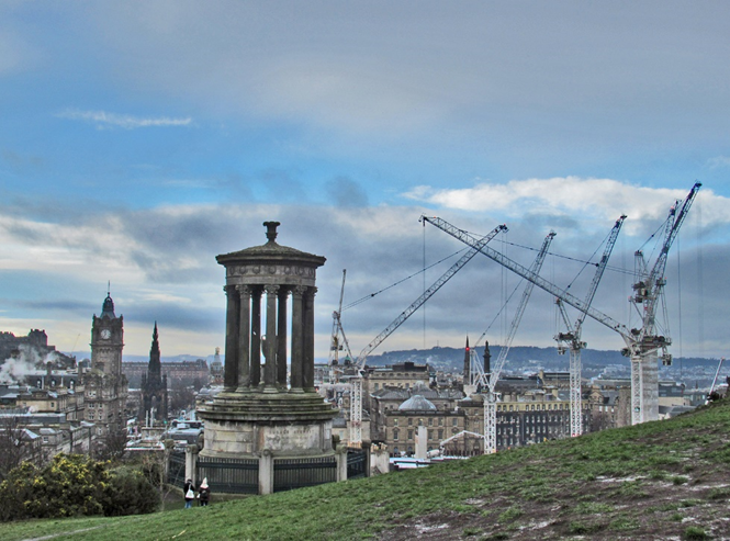 View of Edinburgh looking West towards the castle from Calton Hill. Cranes tower above New Town &  the Dugald Stewart Monument sits in the foreground. 