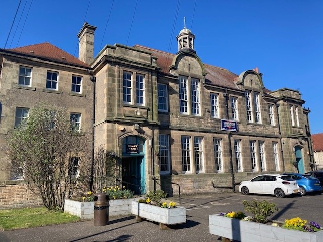 Community Centre, Gilmerton on a sunny day. Three story sandstone community building with parked cars and planters in the foreground