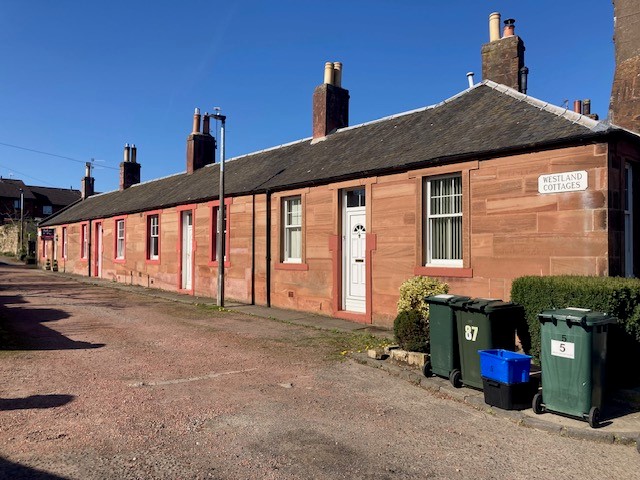 Westland Cottages, Gilmerton on a sunny day - red sandstone single story cottages with a hedge and bins in the foreground.